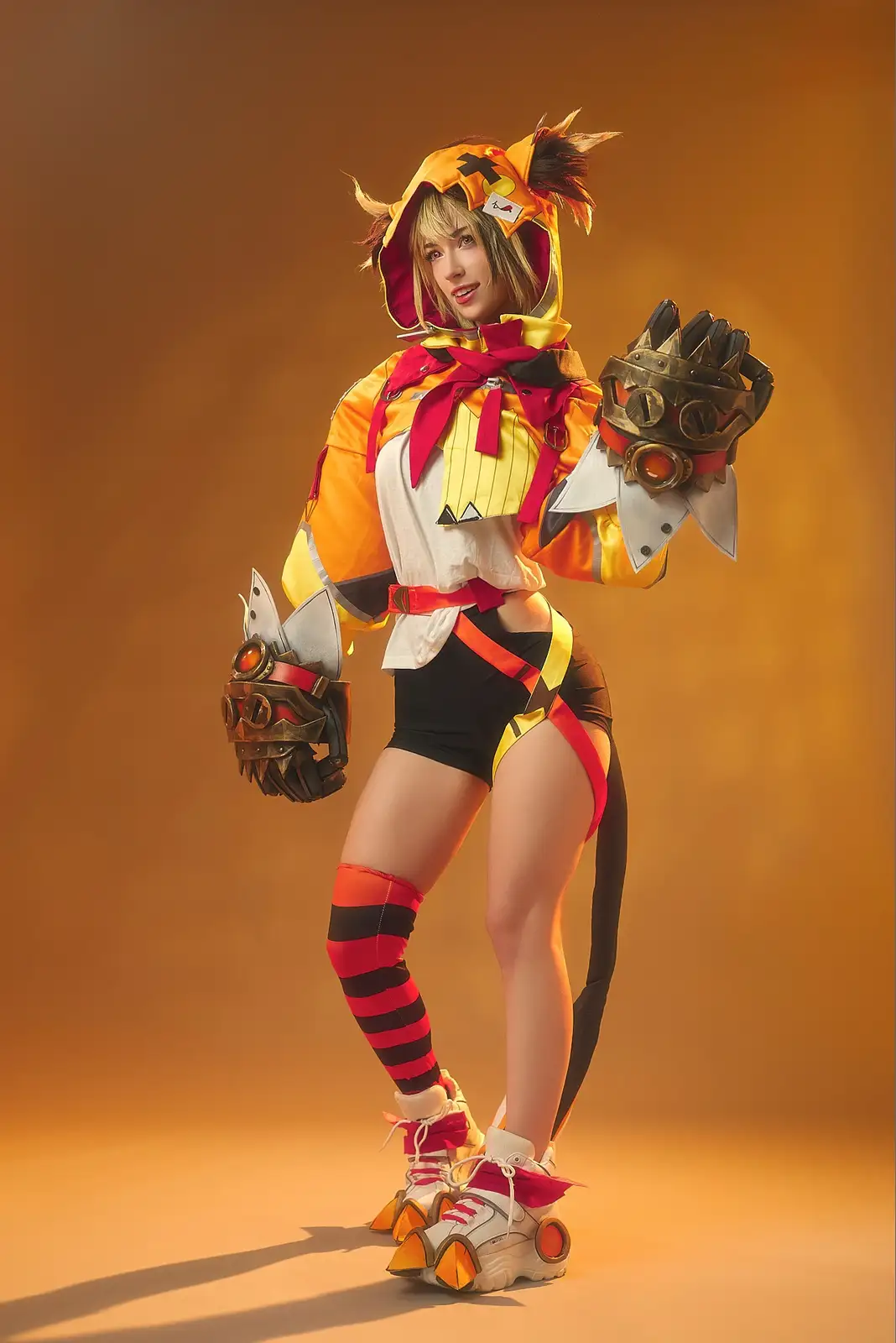 A person in a detailed cosplay of a stylized anthropomorphic cat character, wearing an orange and yellow hooded outfit with…