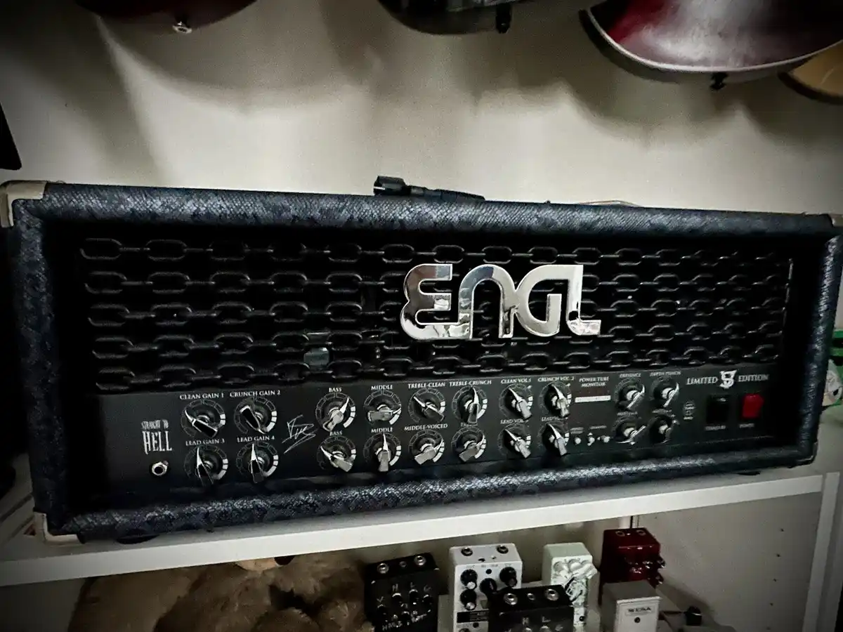 A close-up photo of a black Engl guitar amplifier head with a chain-link grille, multiple knobs for gain, volume, and tone…