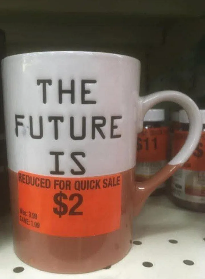 A white ceramic mug with black text reading 'THE FUTURE IS' sits on a store shelf, overlaid with an orange sale sticker that…