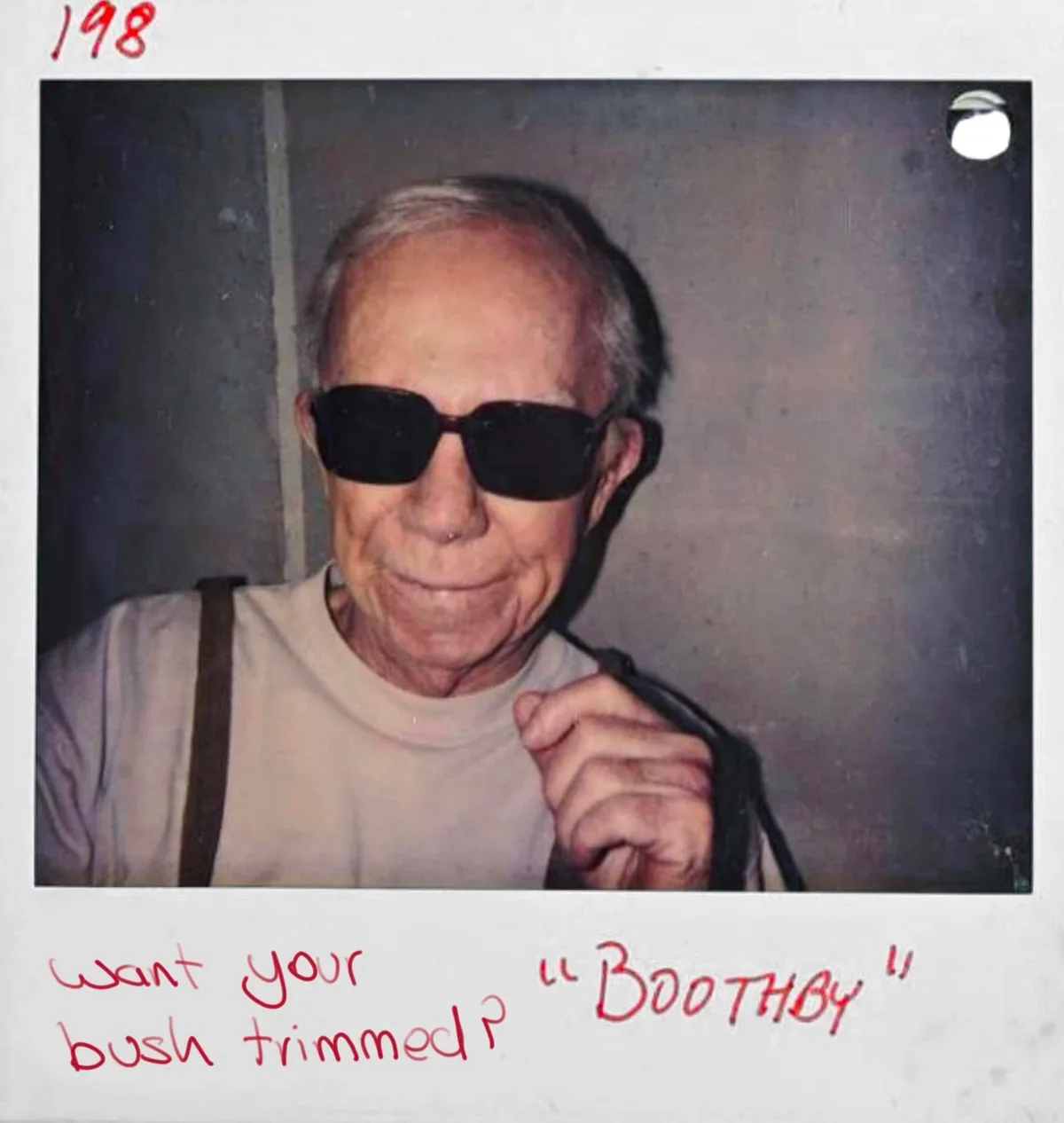 A vintage Polaroid-style photo from 1988 shows an elderly man with sunglasses and a slight smile, holding a strap over his…