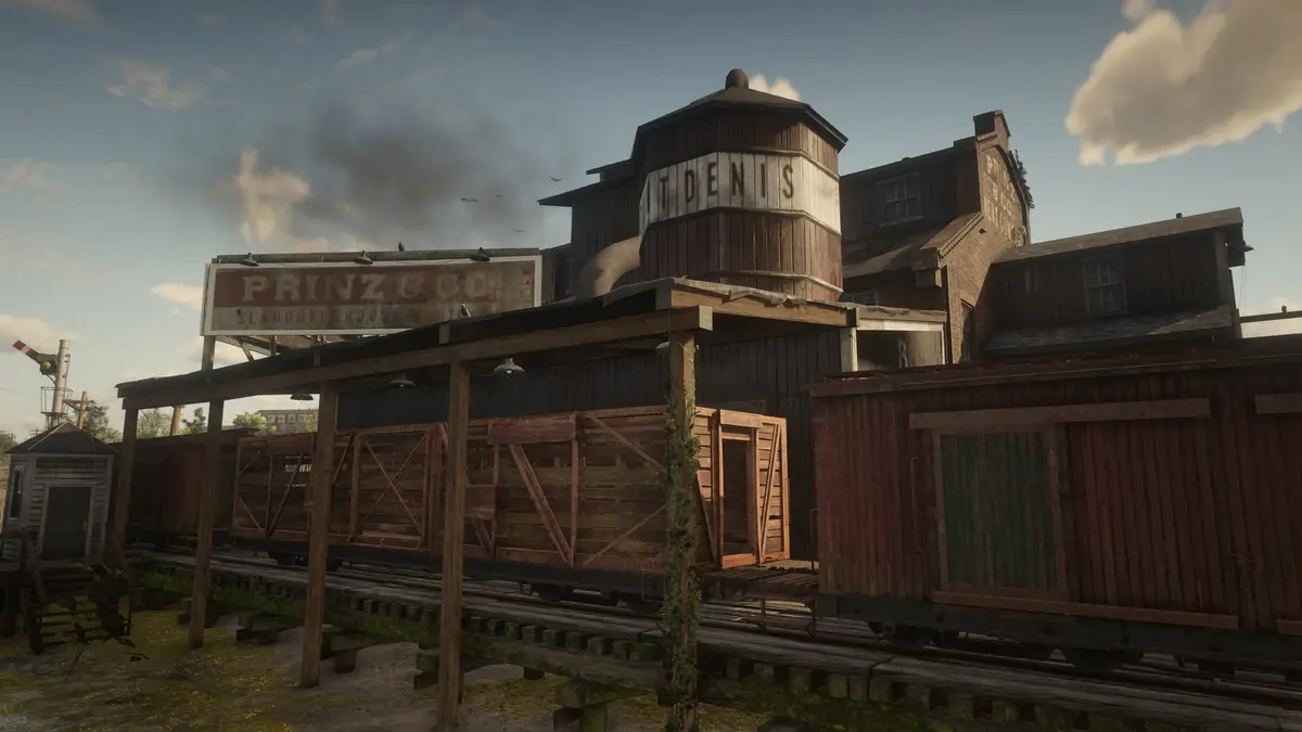 A screenshot from a video game showing a rustic, industrial meatpacking facility with wooden buildings, train cars on…