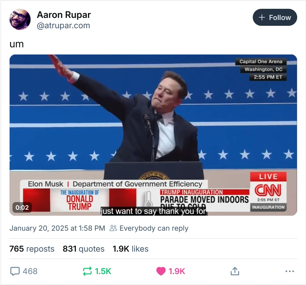 A screenshot of a tweet by Aaron Rupar shows a video clip of Elon Musk at a podium with a blue starry backdrop, appearing to…