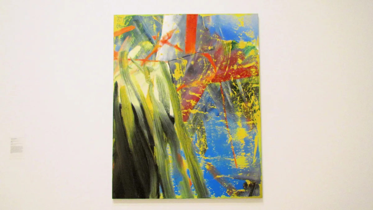 a large abstract painting with bold strokes of green, blue, yellow, and red hangs on a white gallery wall. the overlaid text…