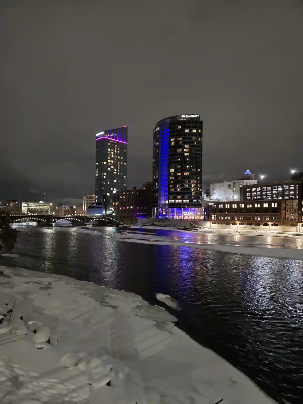 A nighttime cityscape of a snowy riverbank with two prominent skyscrapers, one labeled 'JW MARRIOTT', illuminated with…