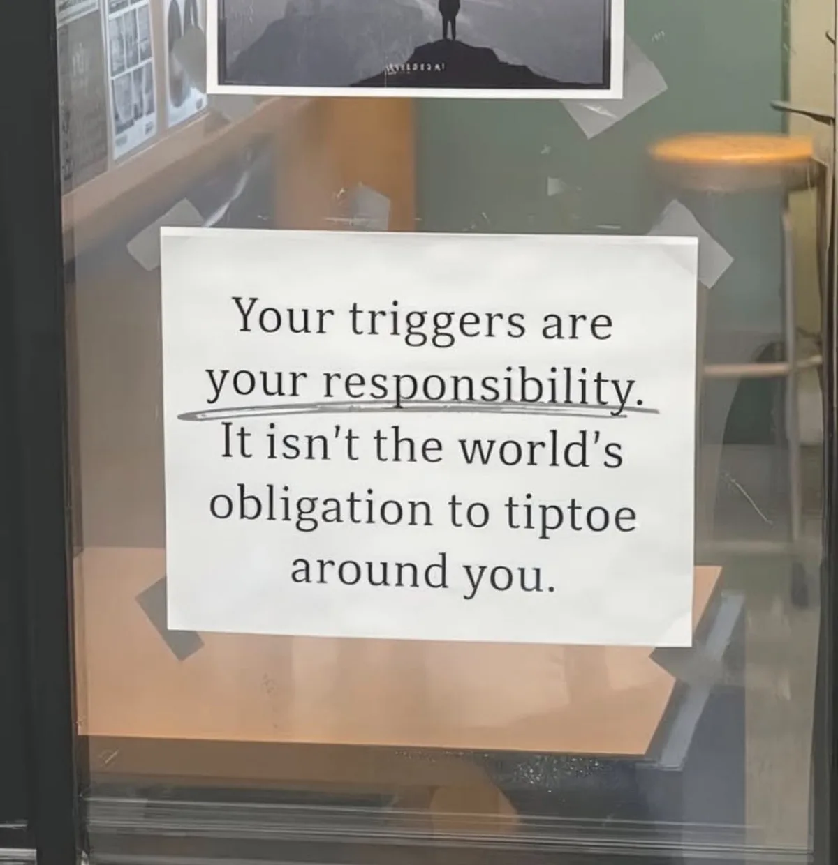 A white paper sign taped to a glass door displays the text 'Your triggers are your responsibility. It isn't the world's…