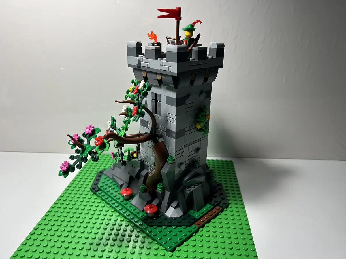 A LEGO castle tower with a tree growing out of its side, featuring flowers and mushrooms at its base, with a minifigure on…
