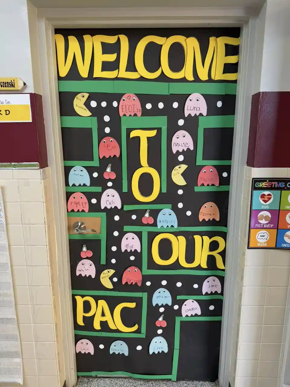 A classroom door decorated with a Pac-Man theme, featuring large yellow letters spelling 'WELCOME TO OUR PAC' against a…