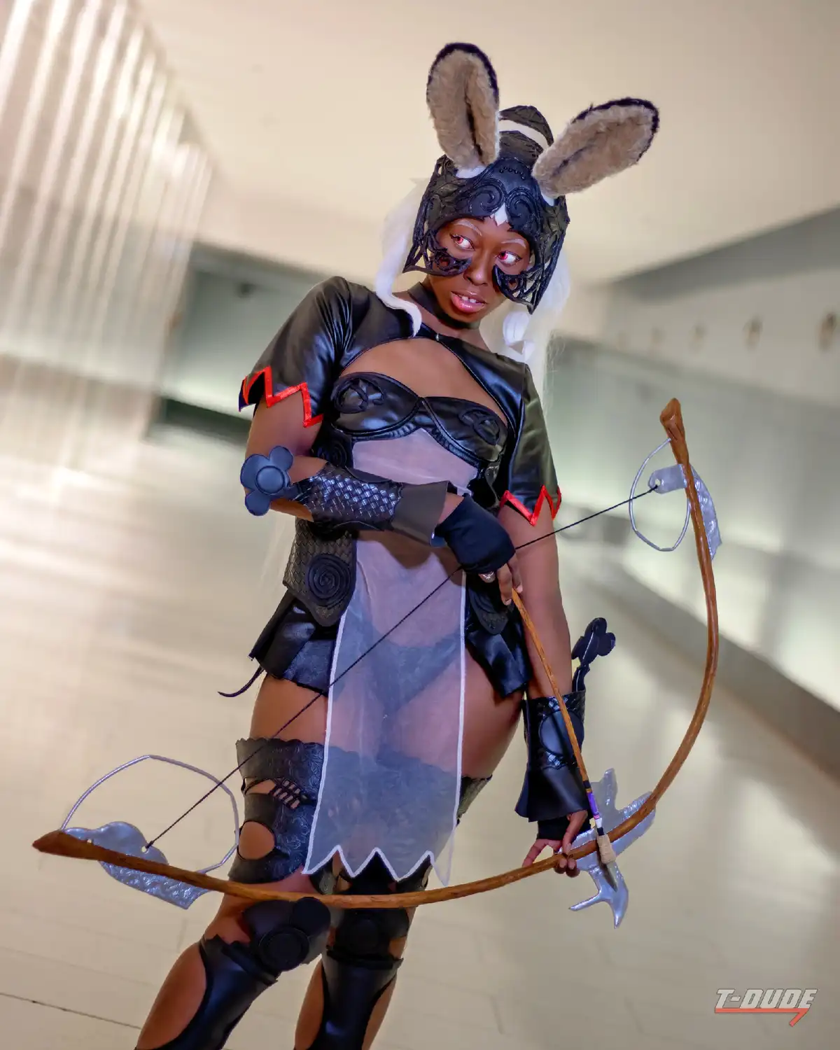A person in a detailed cosplay of a rabbit-themed archer character, wearing a black leather outfit with bunny ears, a mask…