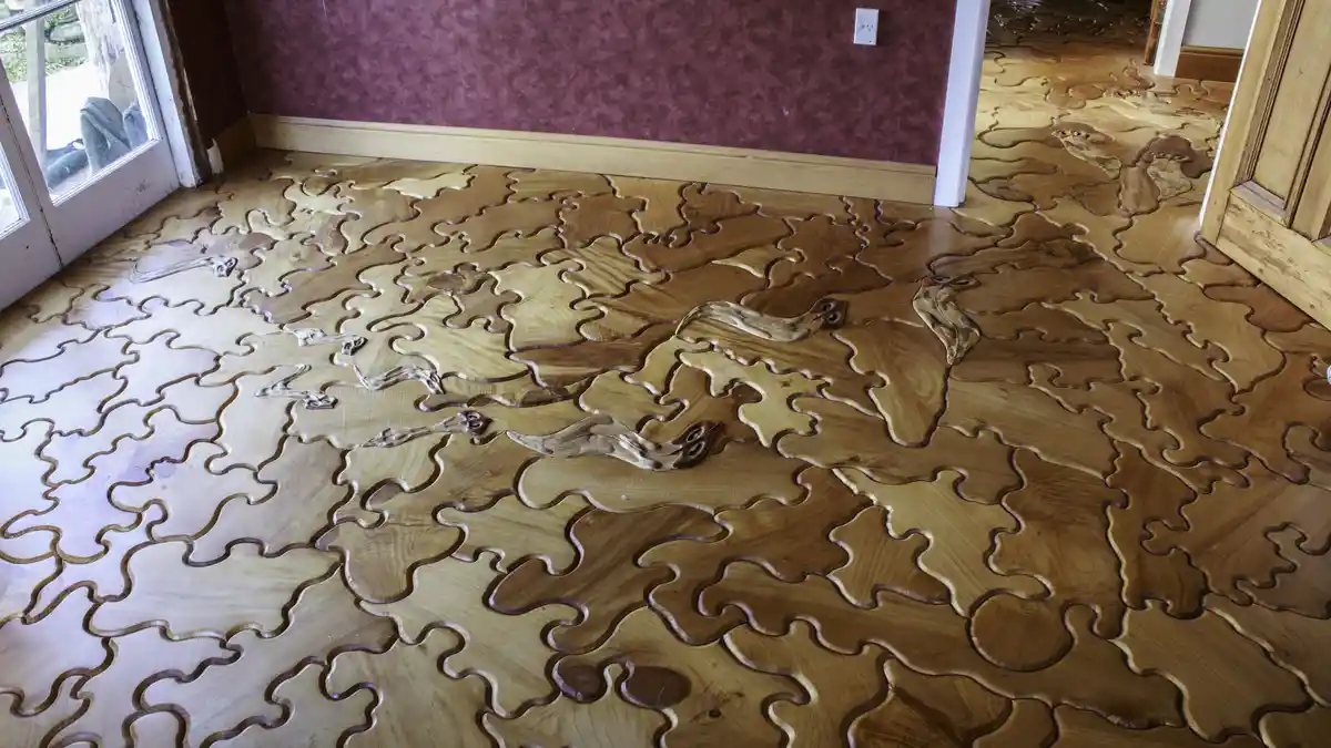 A wooden floor is intricately carved into puzzle-piece shapes, with some pieces appearing to be missing or misaligned…