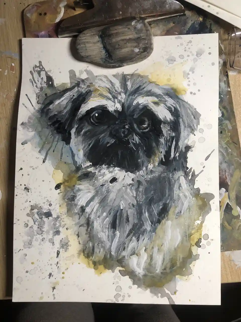 A watercolor painting of a small, shaggy dog with dark eyes and grayish-white fur, rendered on paper with splatters of paint…