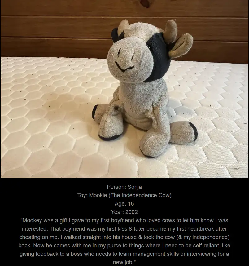 A worn, light gray plush cow toy with black patches sits on a white hexagonal mattress. Text overlaid on a black bar…