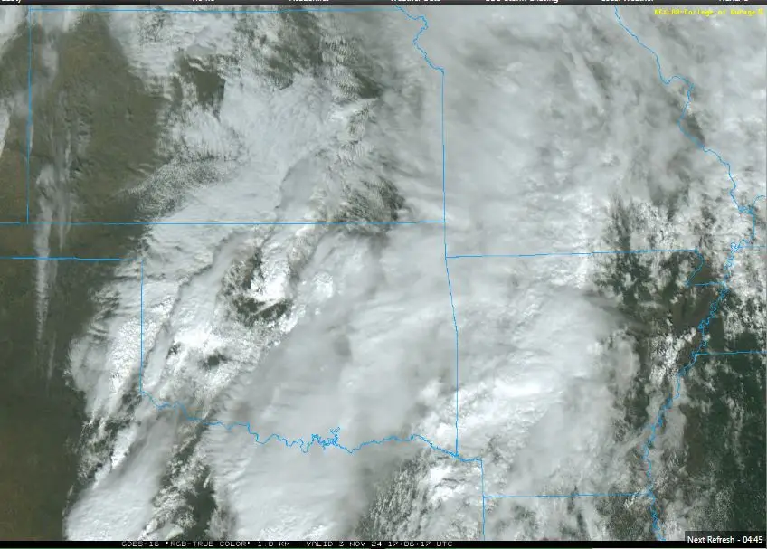 A satellite image shows a large snowstorm system moving over mountainous terrain, with swirling white clouds and snow cover…