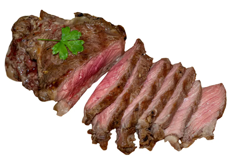 A close-up image of a cooked steak with a green parsley garnish on top, partially sliced into thin pieces revealing a pink…