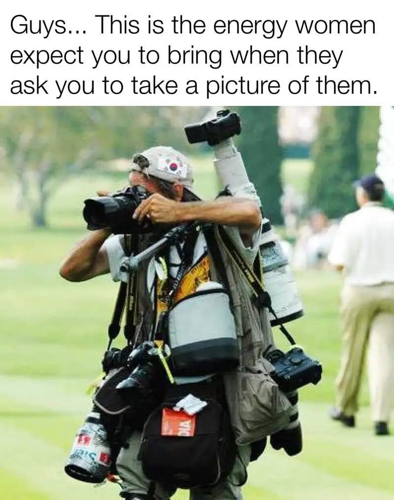 A man is heavily laden with multiple cameras, lenses, and photography gear strapped to his body, holding one camera up to…