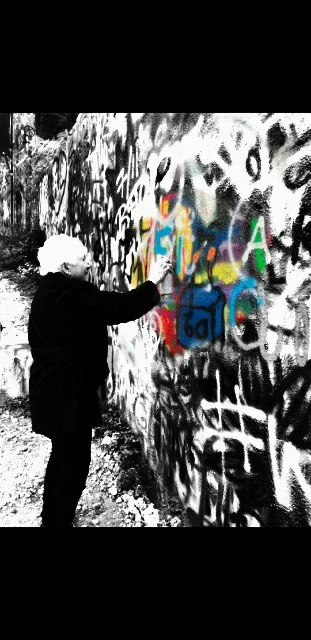 A person in black clothing and a white hat is spray-painting colorful graffiti on a wall already covered in black-and-white…