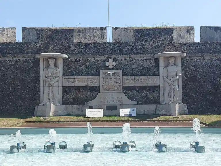 A stone memorial dedicated to Portuguese sailors from the Great War (1914-1918) features two statues of sailors flanking an…