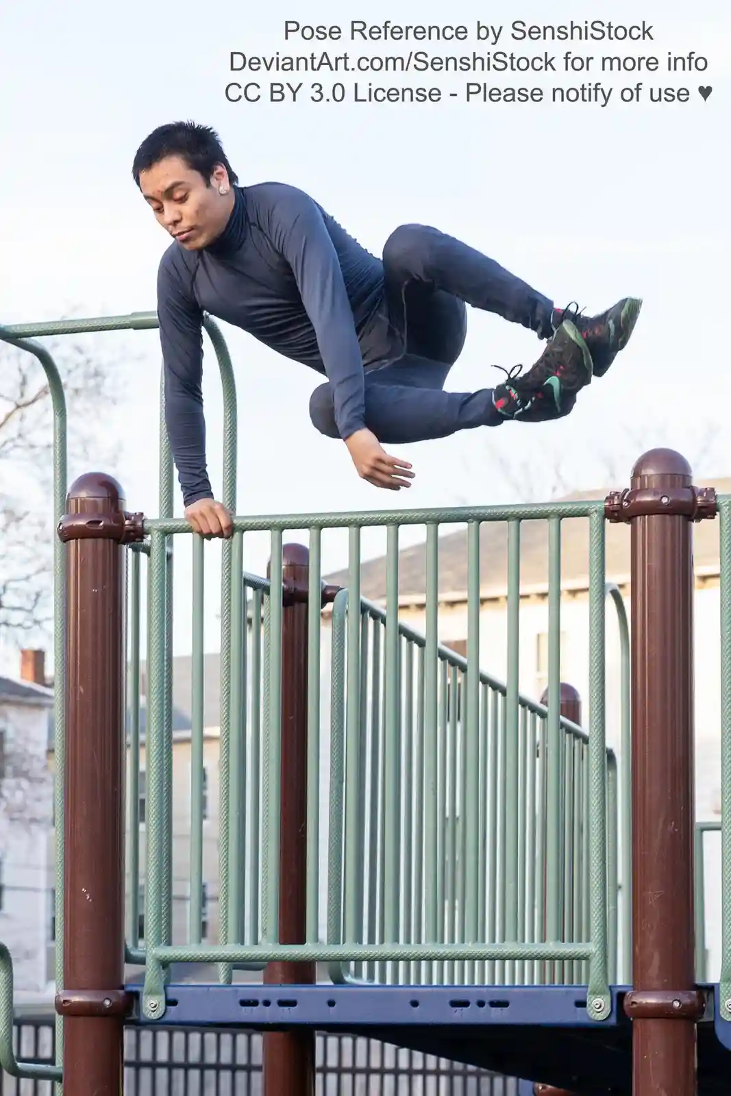 A man in dark athletic wear is captured mid-air, holding onto a green and brown playground railing with one hand while his…