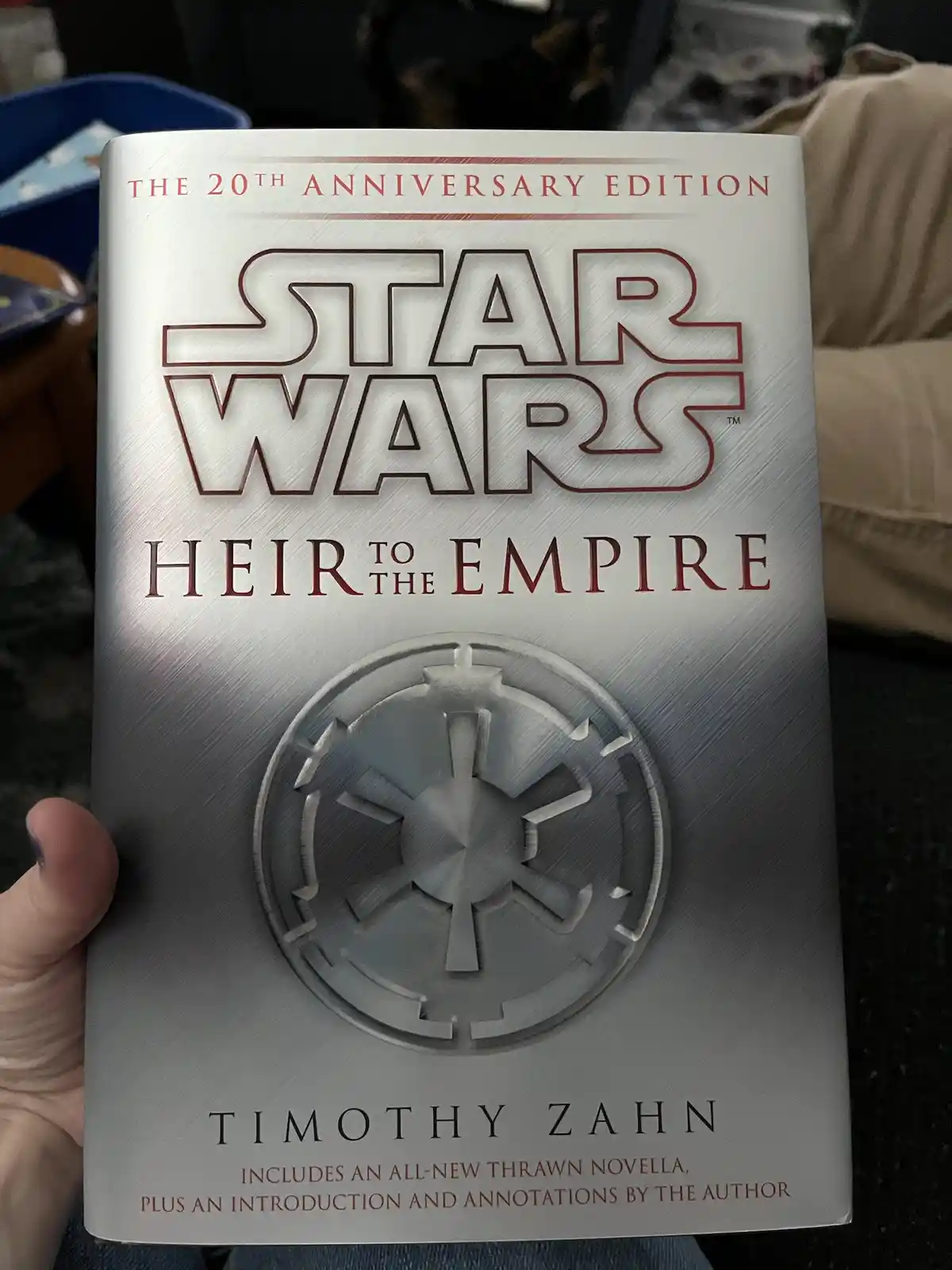 A person holds up a silver-colored book titled 'Star Wars: Heir to the Empire' by Timothy Zahn, labeled as the 20th…