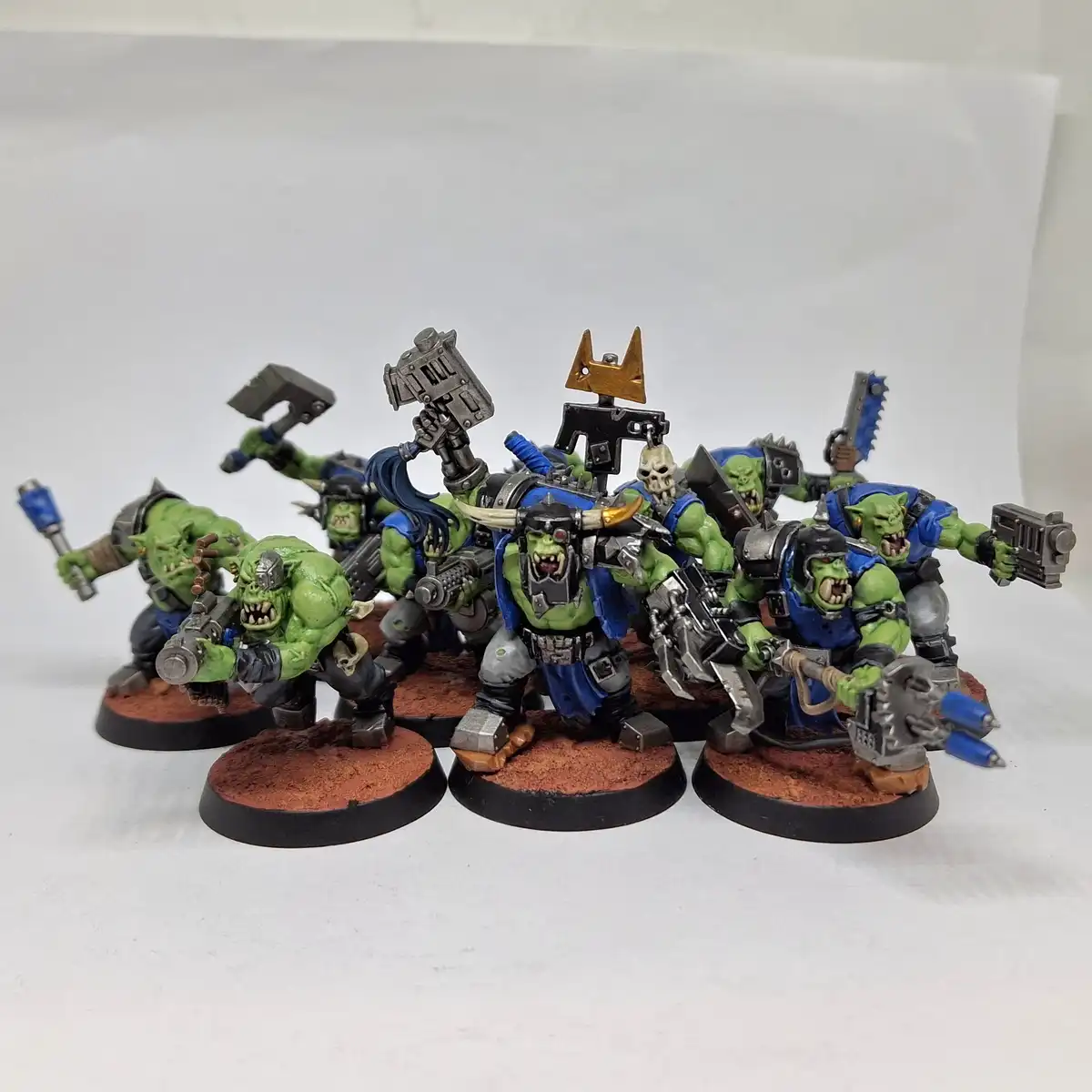 A group of green-skinned, muscular fantasy orcs in blue and grey armor, each wielding various weapons like hammers…
