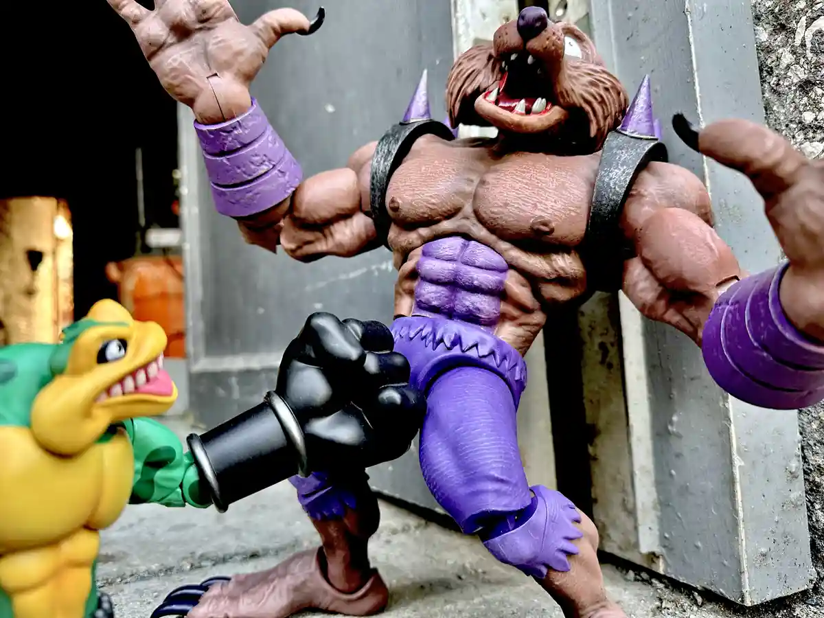 A muscular, brown-furred, anthropomorphic boar action figure with purple armor and spiked shoulder pads is posed…