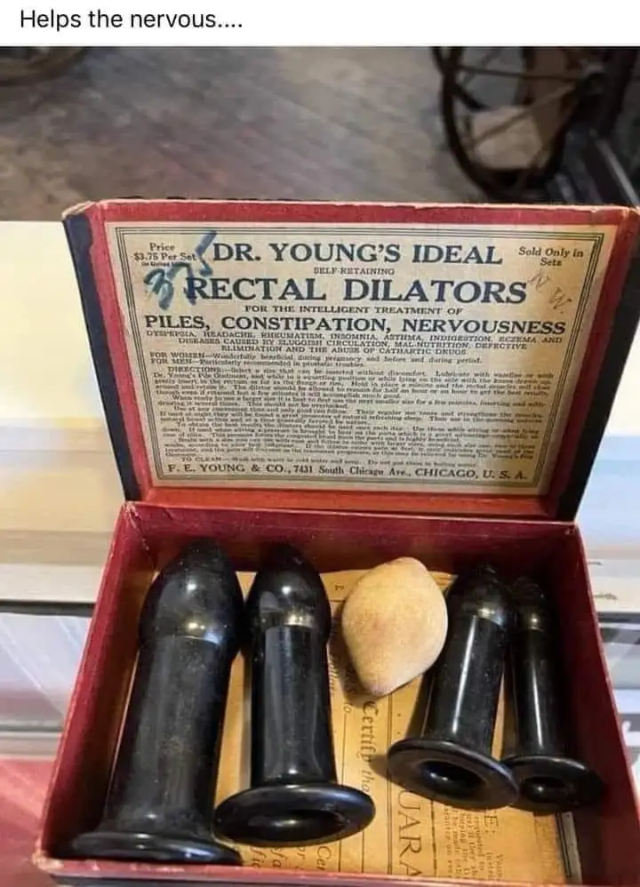 An open red box contains vintage black and white plastic rectal dilators, with a yellowed paper label listing ailments like…