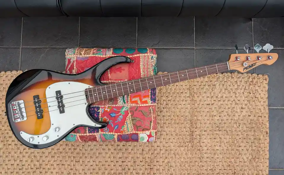 A Penney Milestone III bass guitar with a sunburst finish and white pickguard rests diagonally across a colorful…