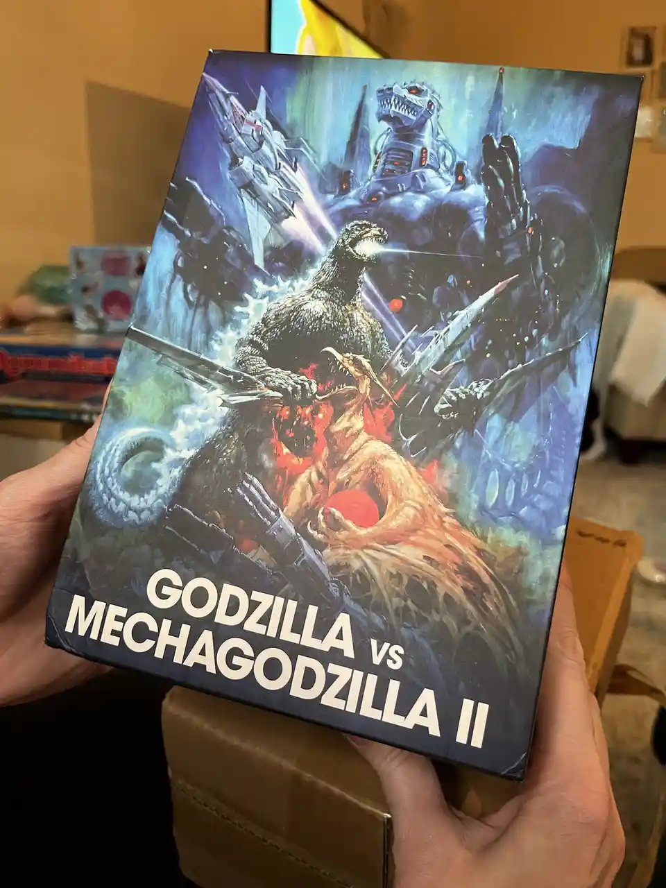 A person holds a box featuring a dynamic illustration of Godzilla battling Mechagodzilla II, with the title 'GODZILLA vs…