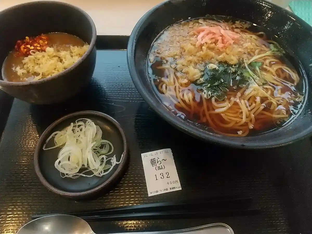 A close-up photo of a Japanese ramen meal on a black tray, featuring a large bowl of noodle soup with toppings like pickled…