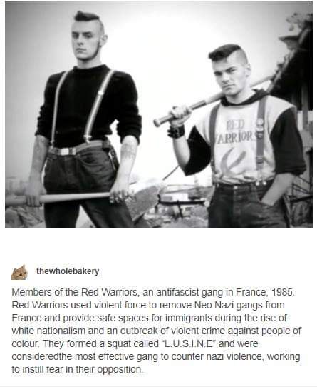 A black-and-white photo shows two young men in 1980s-style clothing, both wearing suspenders and holding baseball bats. The…