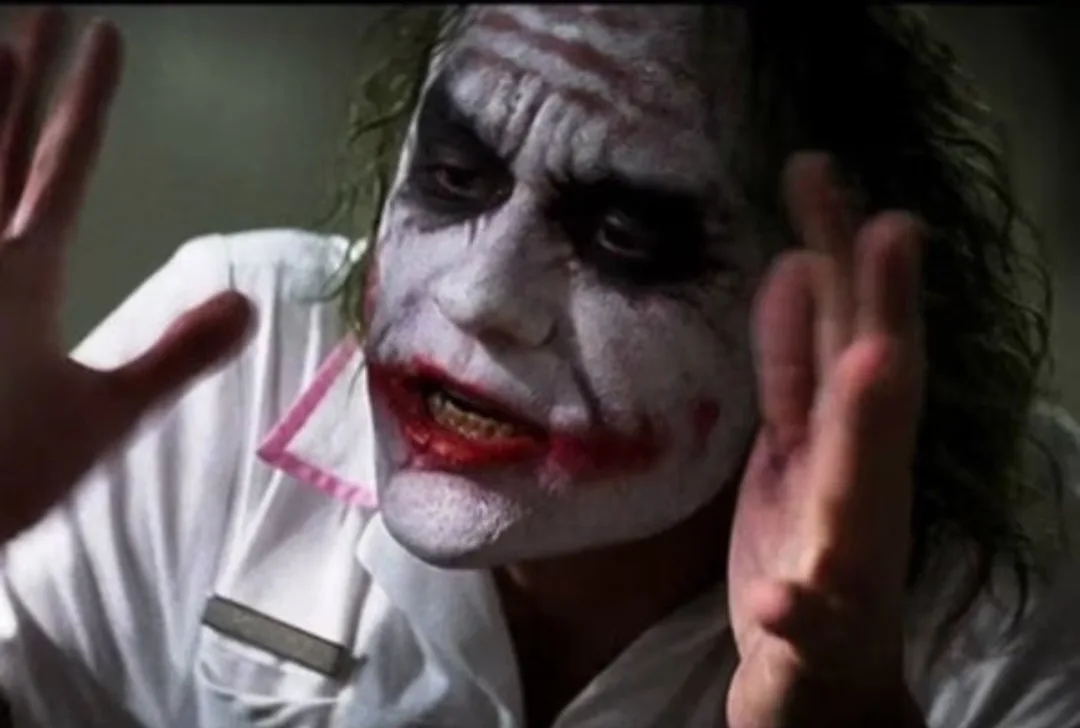 a close-up of the character the joker from the movie 'the dark knight' with white face paint, red lips, and dark eye makeup…