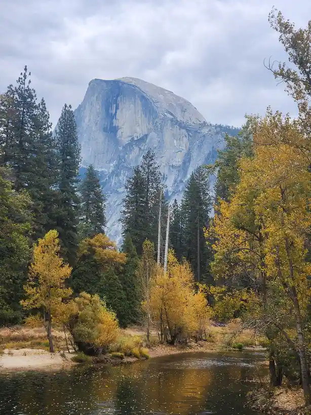 A scenic photo of Half Dome in Yosemite National Park, with autumn-colored trees and a river in the foreground under a…