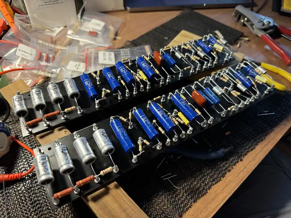 Three black circuit boards are laid out on a workbench, each populated with blue cylindrical capacitors, silver cylindrical…