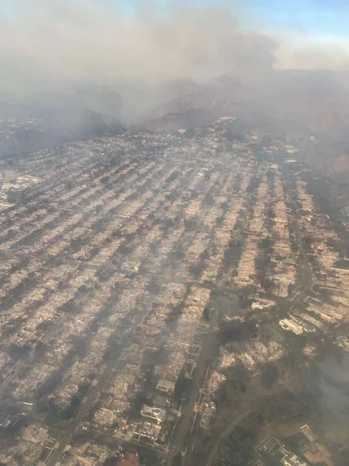 An aerial photograph shows a vast suburban area completely destroyed by fire, with charred remains of homes and streets…
