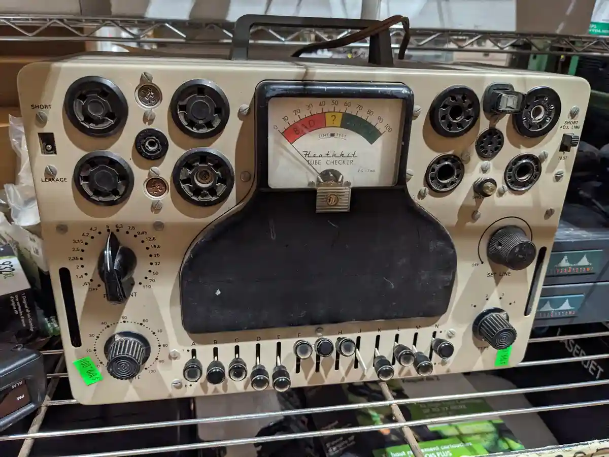 A vintage Heathkit Tube Checker with a needle gauge marked 'BAD', '?', and 'GOOD' sits on a metal shelf, its needle pointing…