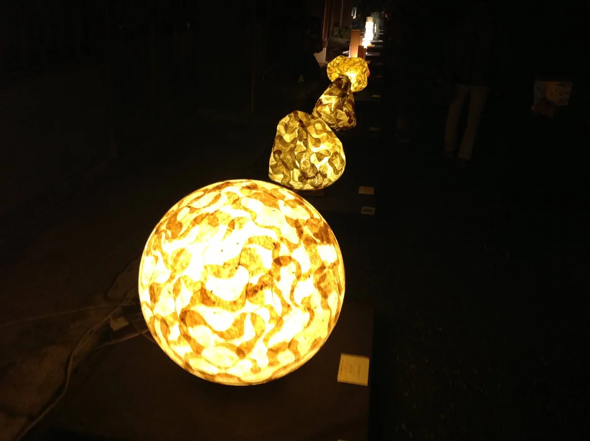 A row of illuminated, textured paper lanterns shaped like planets or celestial bodies, glowing warmly in a dark indoor…