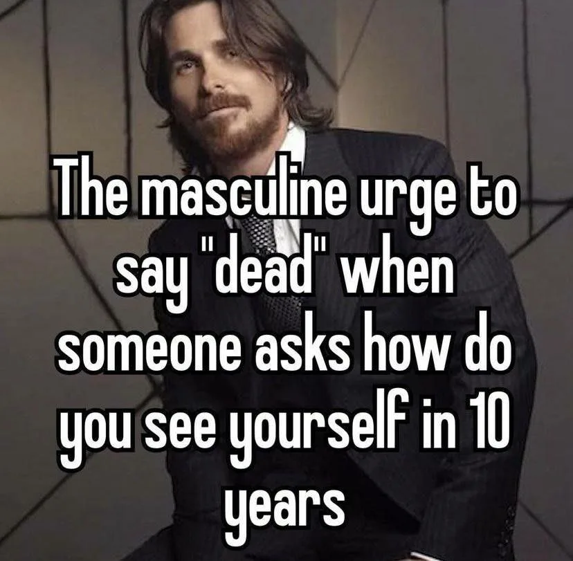 A man with long hair and a beard, wearing a dark suit and tie, looks off to the side with a smug, confident expression…