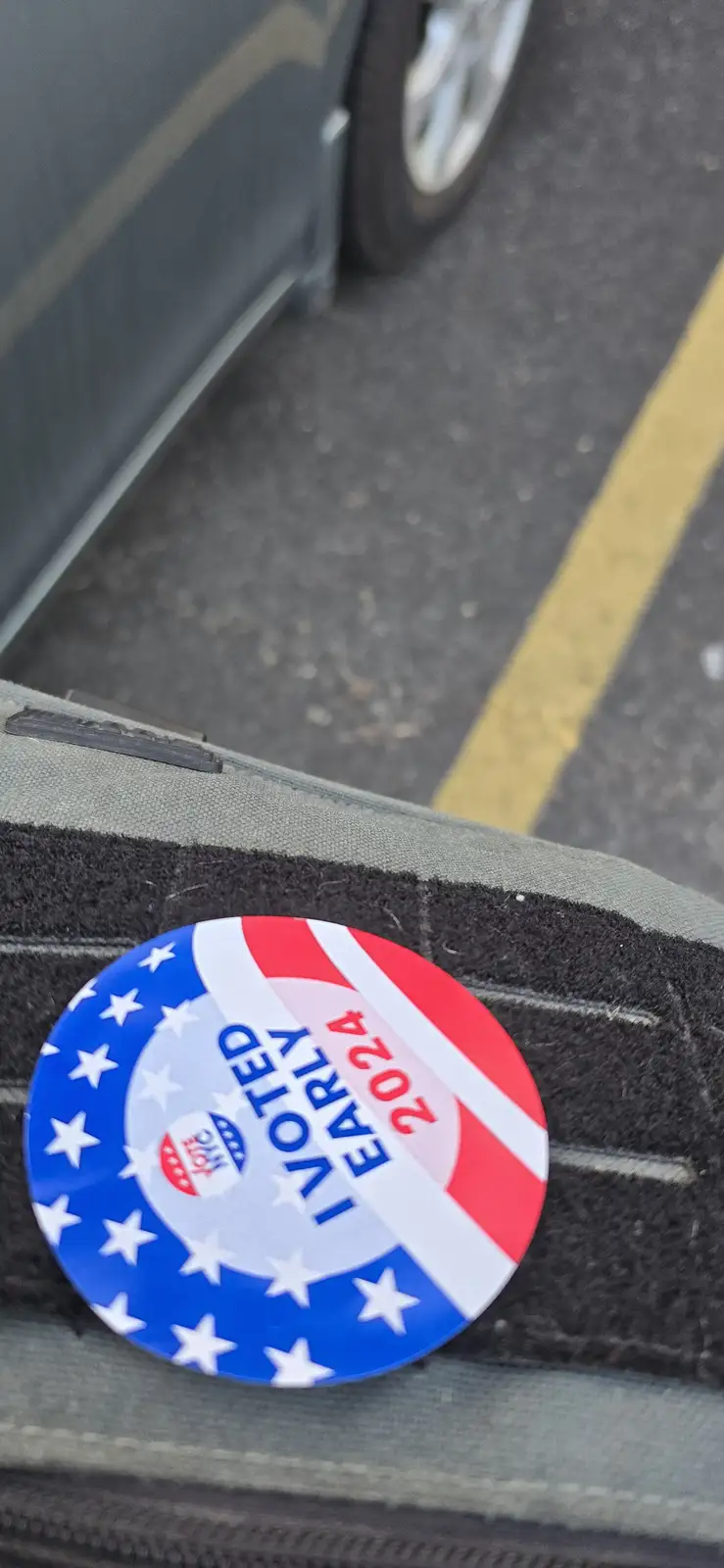 A circular red, white, and blue 'I VOTED EARLY 2024' button with stars and stripes design rests on the textured fabric of a…