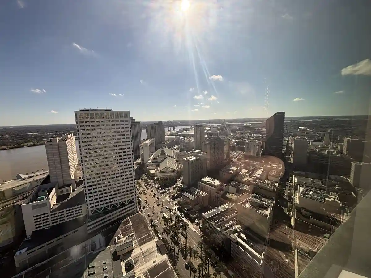 A bright, sun-drenched aerial view of a cityscape with tall buildings, a river, and palm-lined streets, taken from a high…
