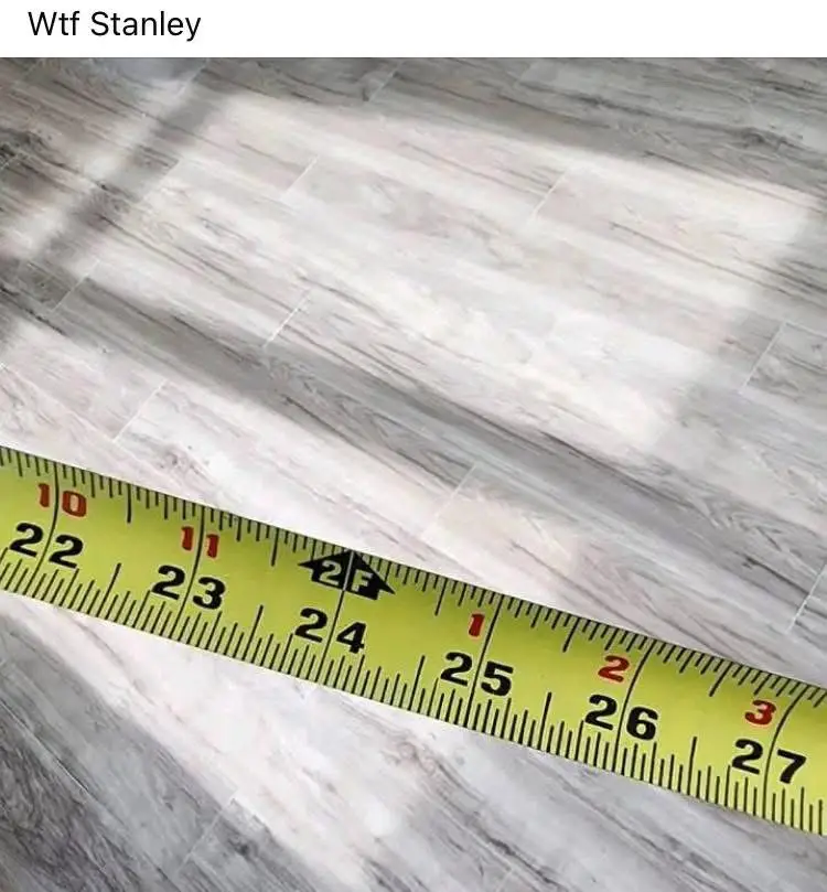 A yellow measuring tape is laid diagonally across a light gray wood-grain laminate floor, with sunlight casting shadows. The…