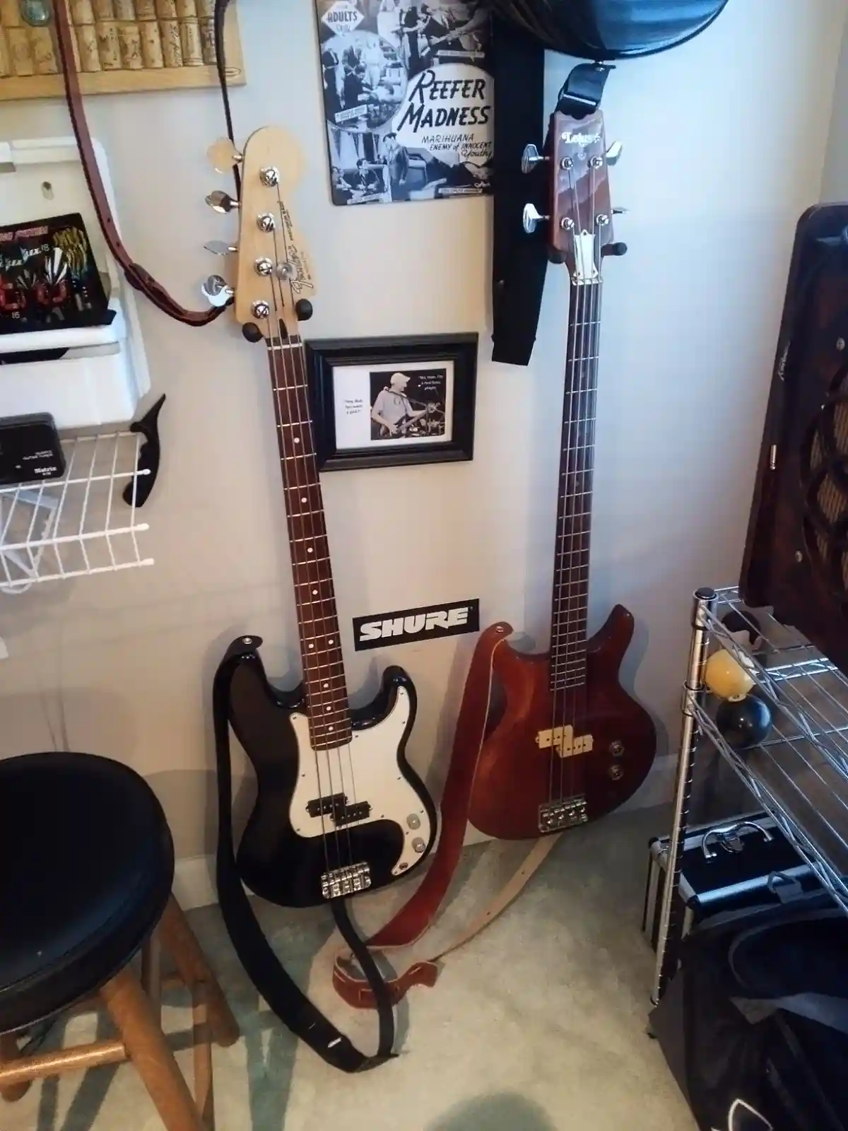 Two bass guitars lean against a wall in a music room, one black and white, one red. Overlaid text reads 'i have two bass…