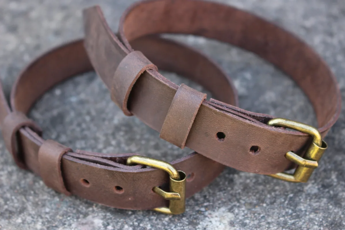 Two brown leather belts with brass buckles lie coiled on a gray concrete surface. The overlaid text reads 'i'm not lazy, i'm…