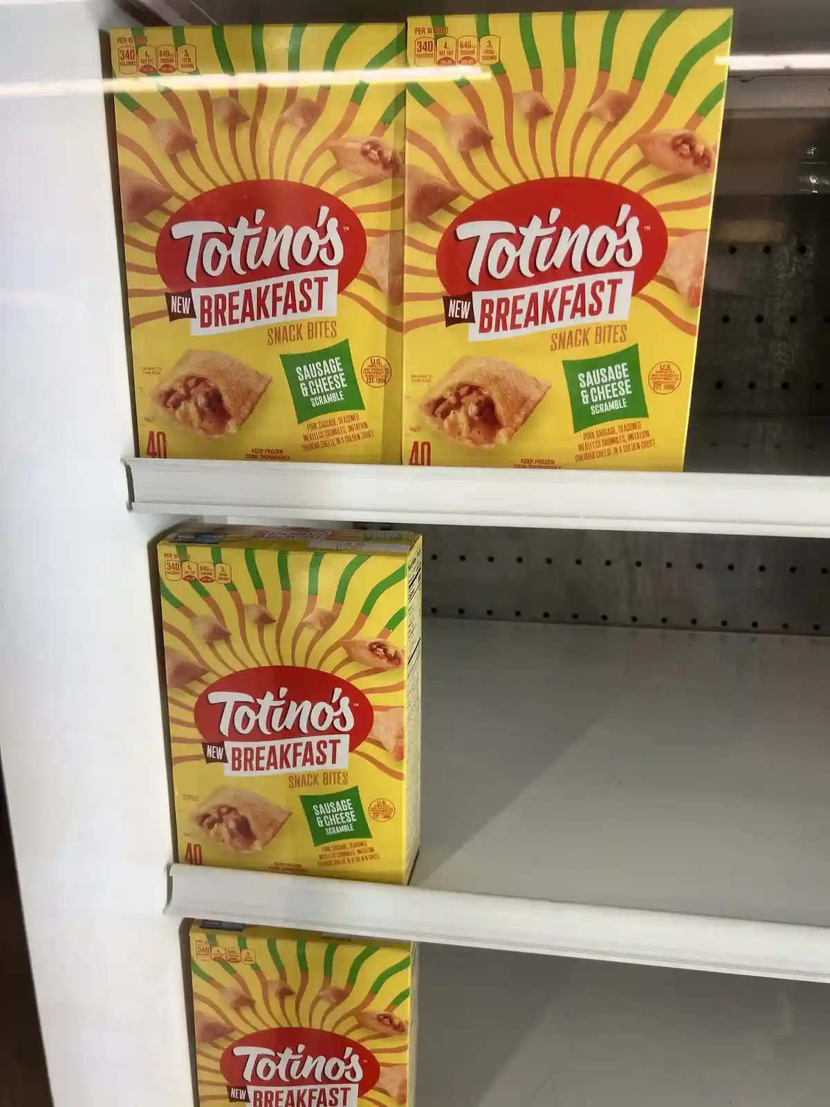 A grocery store freezer shelf displays boxes of Totino's 'New Breakfast Snack Bites' in a 'Sausage & Cheese Scramble'…