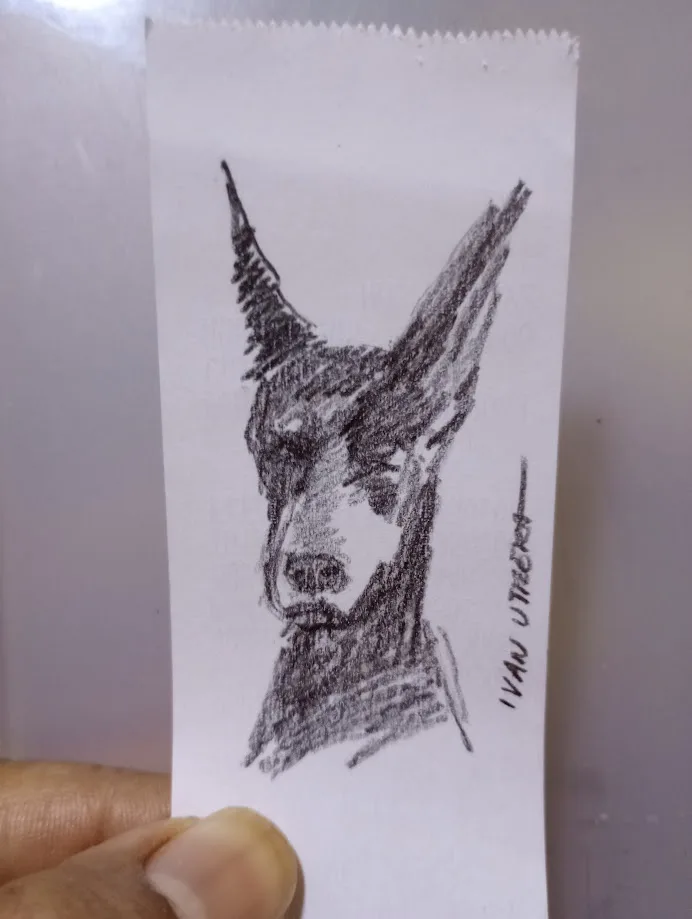 A hand holds a small, vertically oriented sketch on white paper, depicting a stylized dog's head with pointed ears and a…