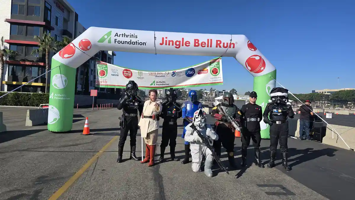 A group of Star Wars cosplayers, including Darth Vader, Boba Fett, and Stormtroopers, pose under a large inflatable archway…