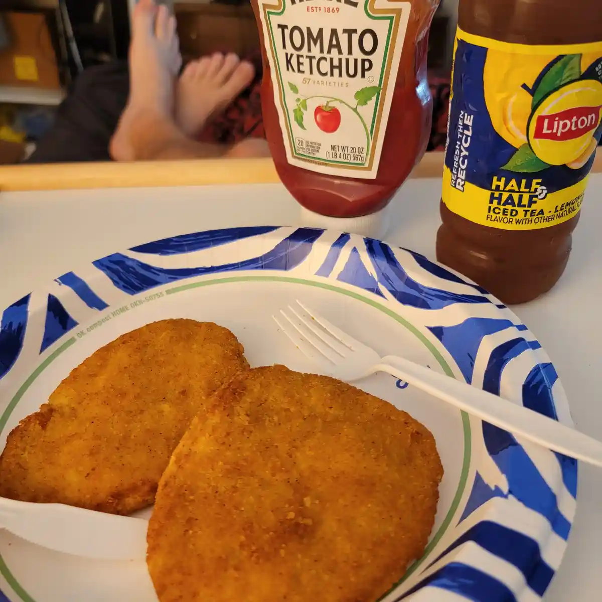 A close-up shot shows two golden-brown breaded chicken nuggets on a blue and white patterned paper plate with a white…