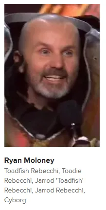 A close-up image of actor Ryan Moloney smiling while wearing a futuristic, armored costume with a helmet partially visible…