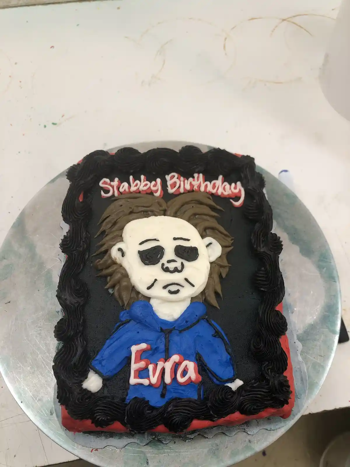 A rectangular birthday cake decorated with frosting to resemble the character Michael Myers from Halloween, featuring a…