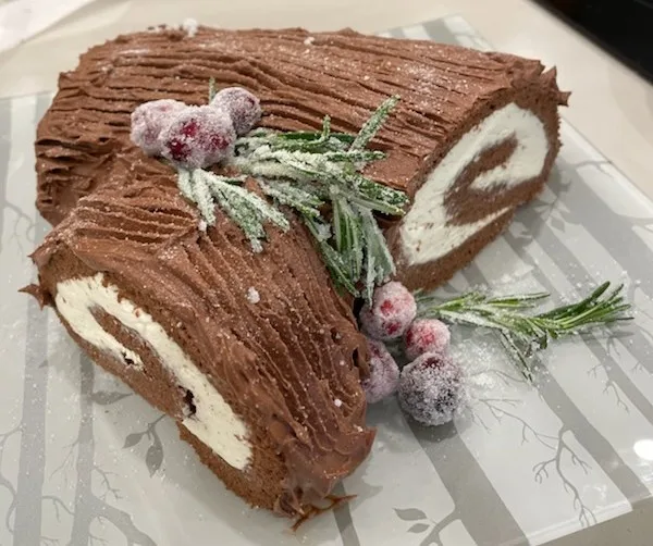 a chocolate cake rolled into a log shape, decorated with sugared cranberries and rosemary sprigs to mimic a Christmas tree…