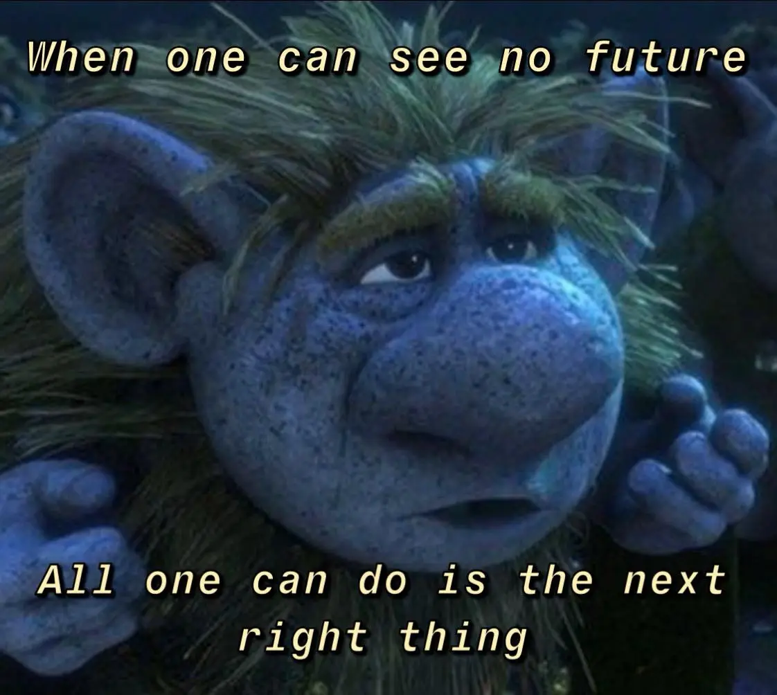 A close-up of a blue-skinned, furry troll character with a sad, resigned expression, looking upward. The image has two lines…