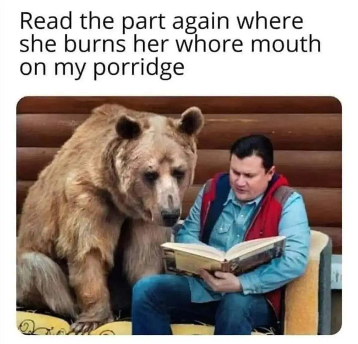 A man in a blue shirt and red vest sits on a couch reading a book, while a large brown bear sits beside him, looking…